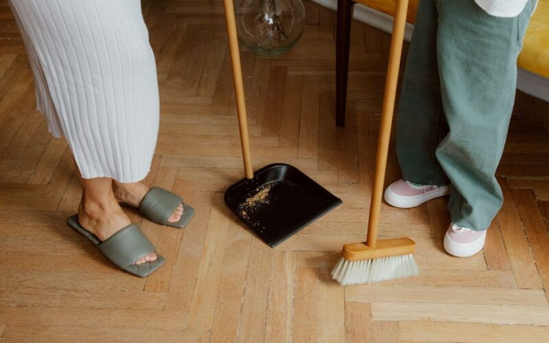 A mother and child cleaning the floor with a broom and dustpan indoors.