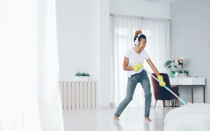 Young woman cleaning indoors with headphones, enjoying music while mopping.