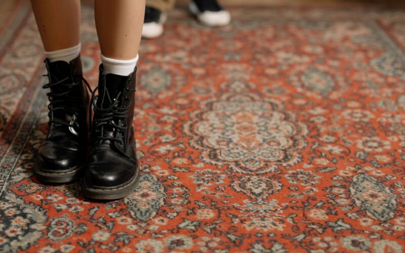 Detail shot of black leather boots on a floral-patterned Persian carpet indoors.