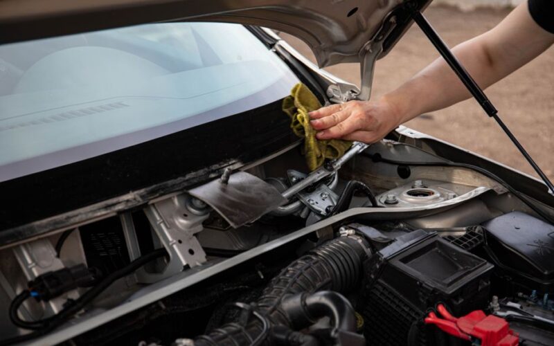 A mechanic wipes the windshield of a car, focusing on engine and windshield maintenance.