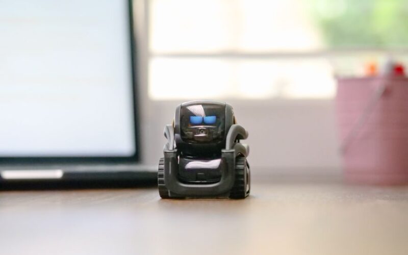 Small toy robot on a desk beside a laptop, symbolizing technology and innovation.