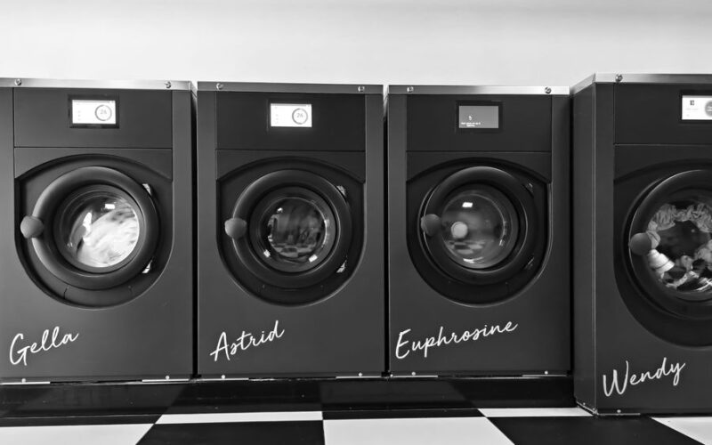 Grayscale image of four modern washing machines in a self-service laundry.