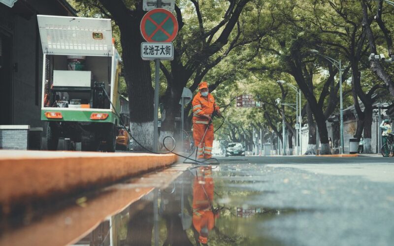 Street cleaner using power spray on a wet Beijing street with reflections.