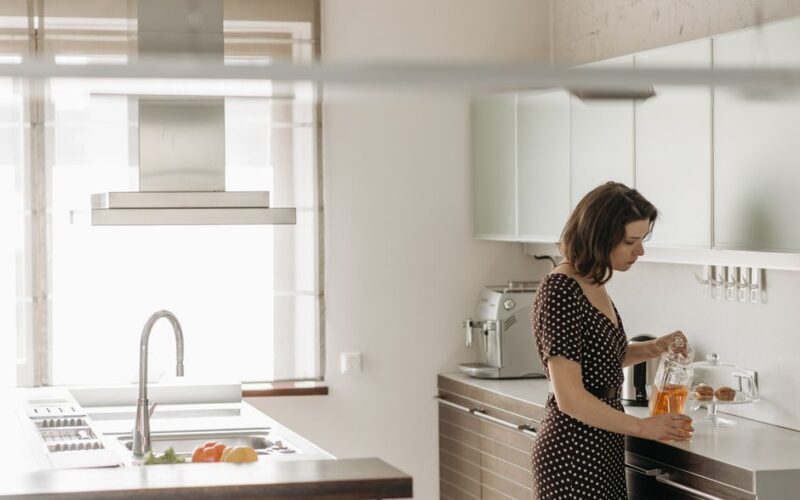 A woman in a polka dot dress pours juice in a contemporary kitchen, showcasing a clean and modern interior design.
