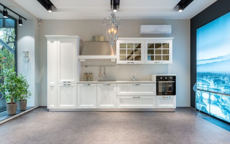Elegant white classic styled furniture and modern appliances in spacious light kitchen with screen and panoramic window