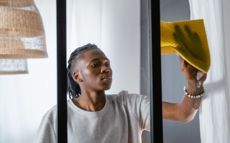 A man cleaning a window with a yellow towel, focusing on indoor chores.