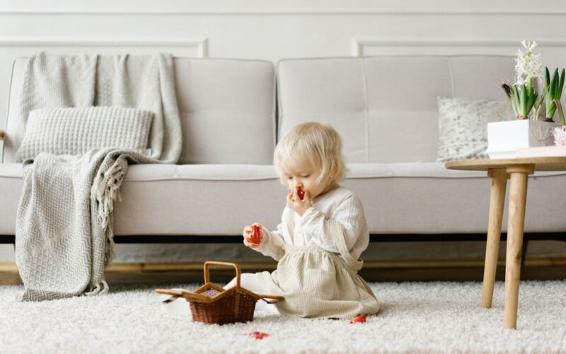 A toddler sits on a cozy rug eating strawberries in a bright living room.