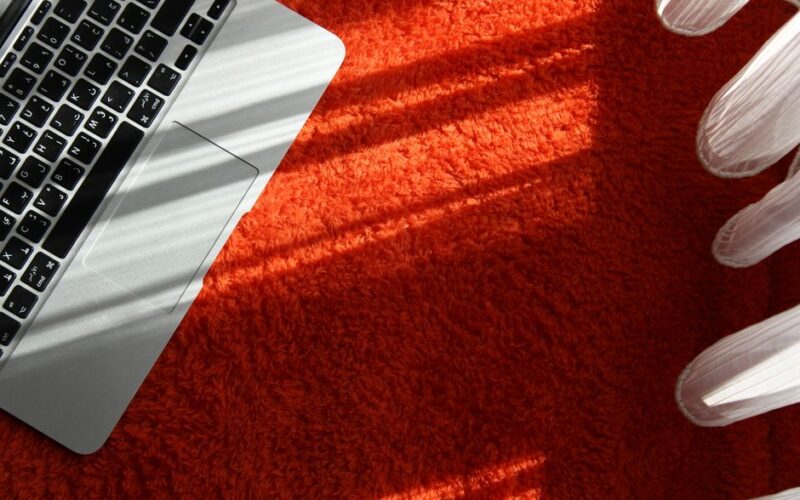 A close-up of a laptop on an orange carpet with sunlight casting shadows, symbolizing technology and creativity.