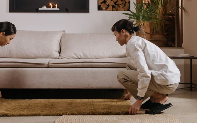 A couple arranging a rug in a stylish, cozy living room with elegant decor and plants.