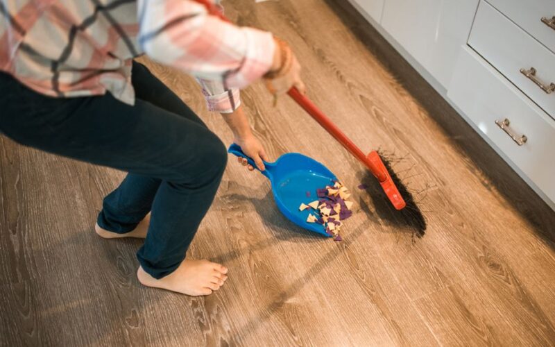 Close-up of a person sweeping debris into a blue dustpan on a wooden floor.