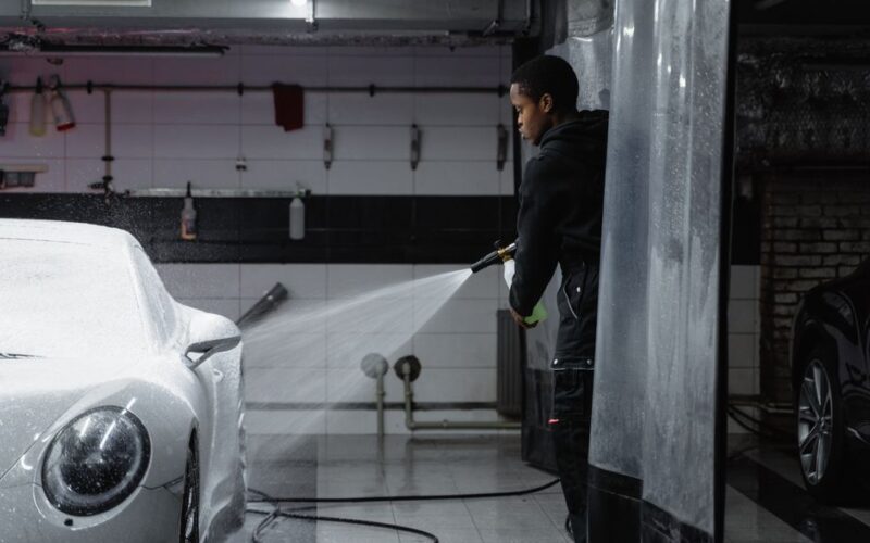 A person using a pressure washer to clean a car in an indoor garage setting.