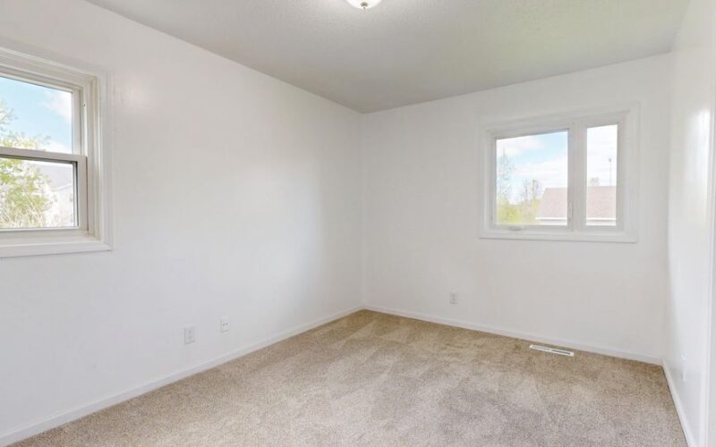 Spacious empty room with two windows, white walls, and neutral carpet flooring, ideal for real estate listings.