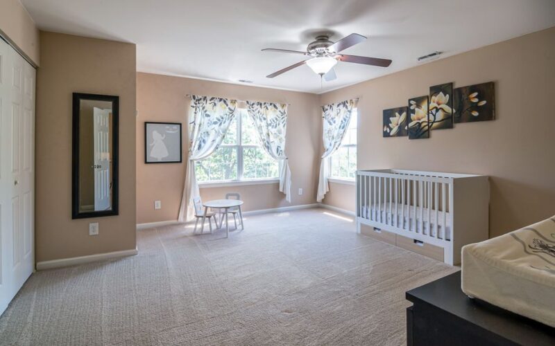 Spacious nursery room featuring a crib, decor elements, and soft carpeting in a serene setting.