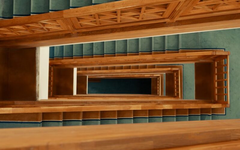 An intriguing view of a wooden staircase with teal carpet, captured from above, showcasing geometric symmetry.