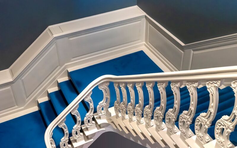 A beautifully detailed white staircase adorned with a vibrant blue carpet in an indoor setting.