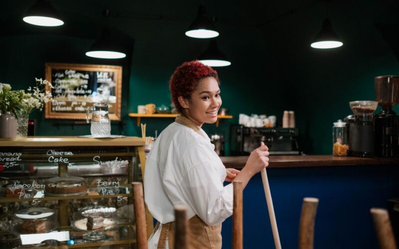 Smiling female barista in a cozy cafe cleaning while surrounded by delicious pastries.
