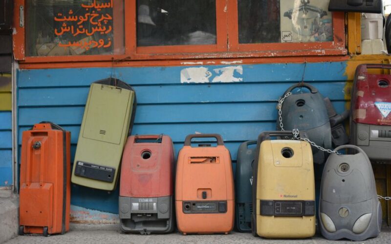 A row of colorful vintage vacuum cleaners displayed against a blue wall in Tehran, Iran.