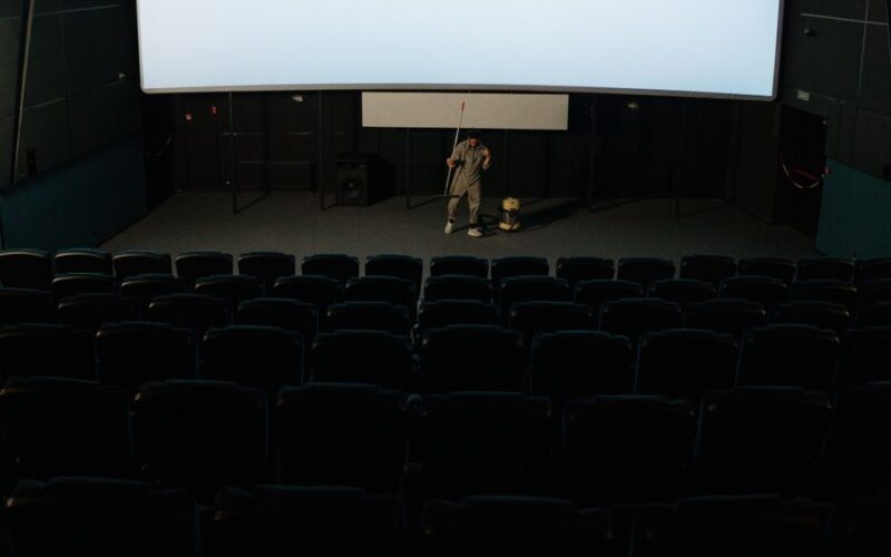 A custodian cleaning an empty cinema auditorium after a movie showing.