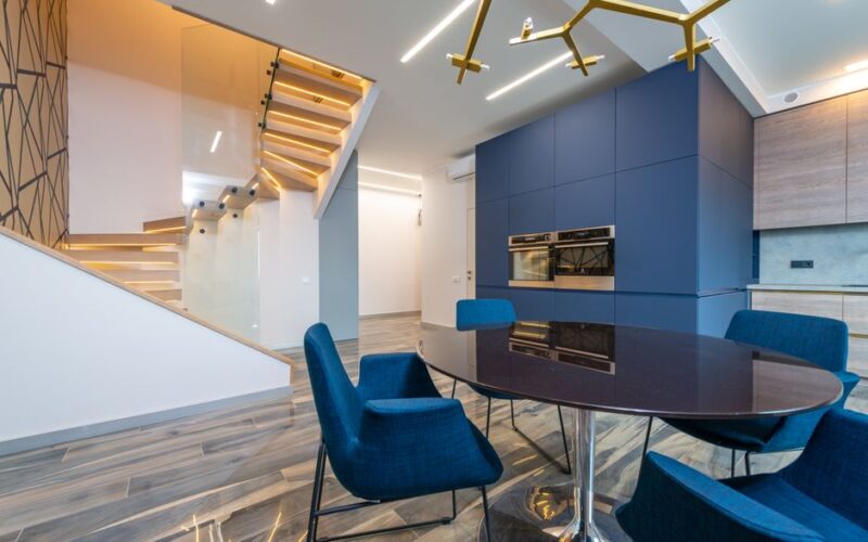 Contemporary kitchen with table and armchairs against built in electric appliances and stairs in light house