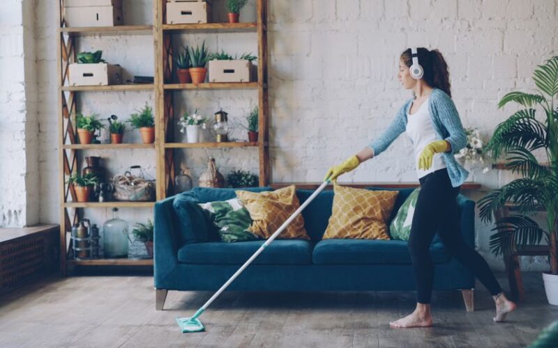 Woman wearing headphones and gloves while mopping a stylish indoor living room.