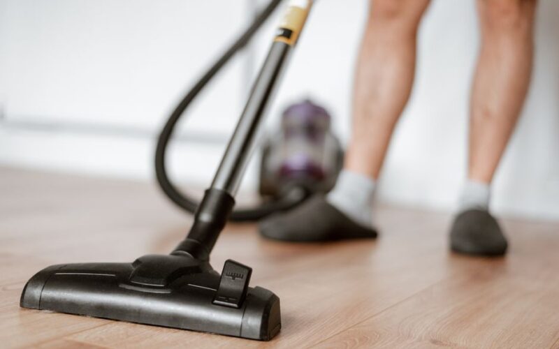 Crop anonymous male in slippers washing floor with vacuum cleaner in flat during household routine