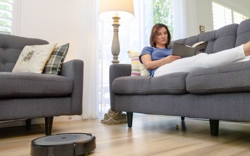 Woman reading on sofa while a robovac cleans the hardwood floor in a modern living room.