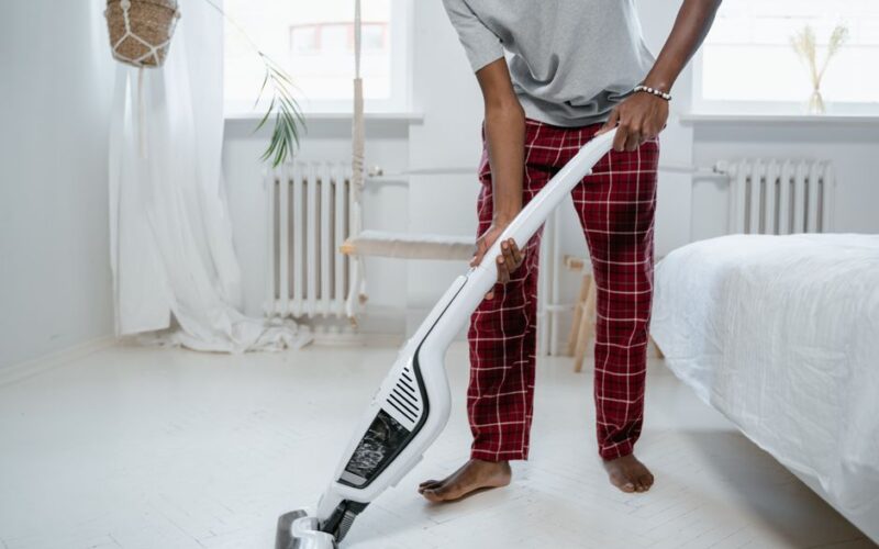 A person cleaning a bedroom with a modern vacuum cleaner, showcasing casual home lifestyle.