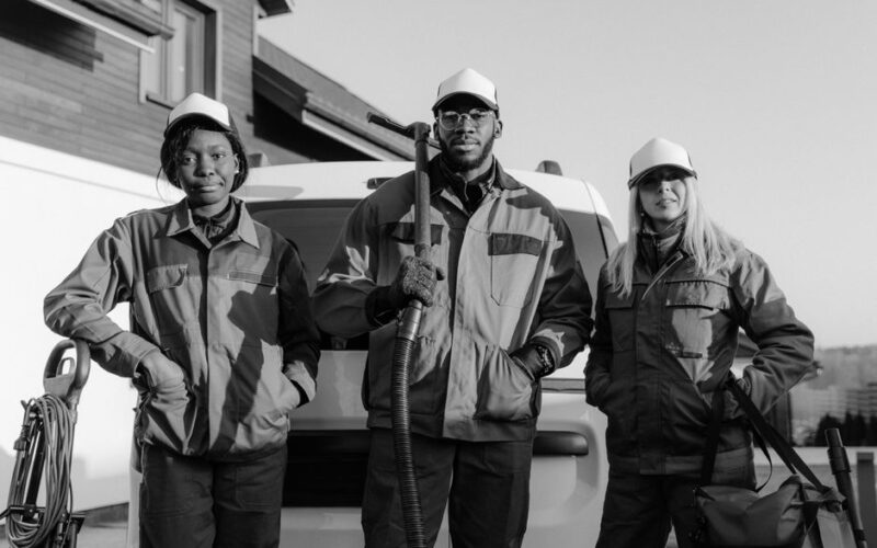 Three professional cleaners in uniform pose with equipment in front of a building.