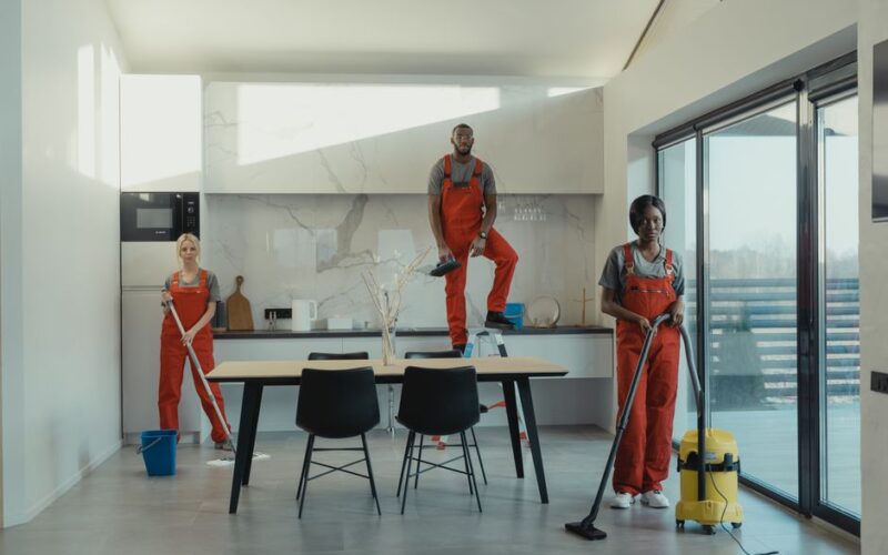 Three cleaning staff working in a contemporary kitchen setting, showing teamwork and efficiency.