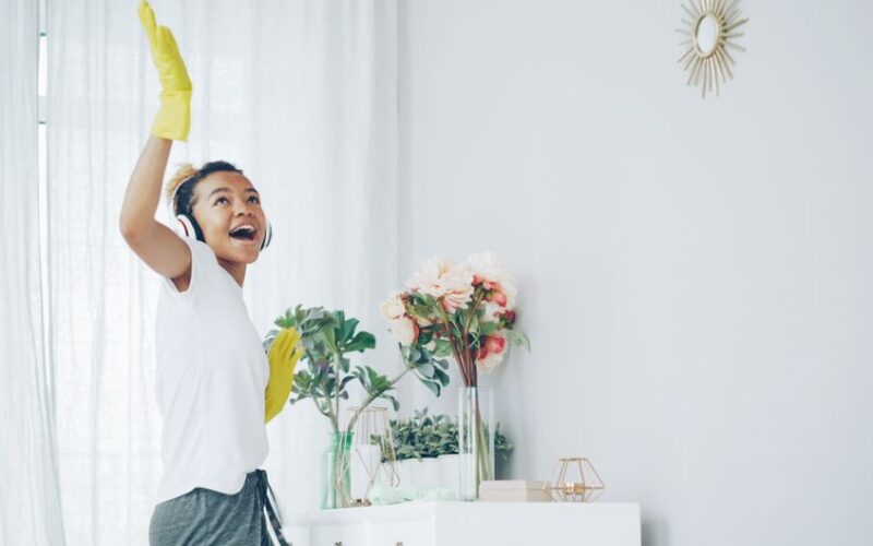 Happy woman with headphones dances while cleaning a bright, stylish room.