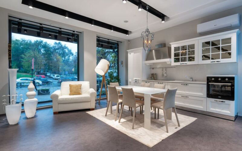Comfortable armchair and dining table with chairs placed in spacious kitchen with classic styled white cupboards and modern appliances
