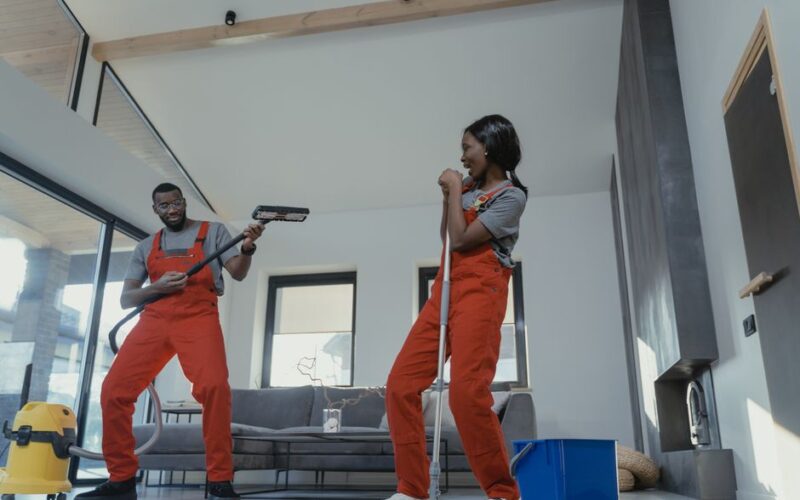 Two adults in vibrant coveralls cleaning a modern home interior, enjoying work.