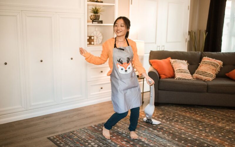 Asian woman happily cleaning her living room with a vacuum. Bright, cheerful indoor setting.