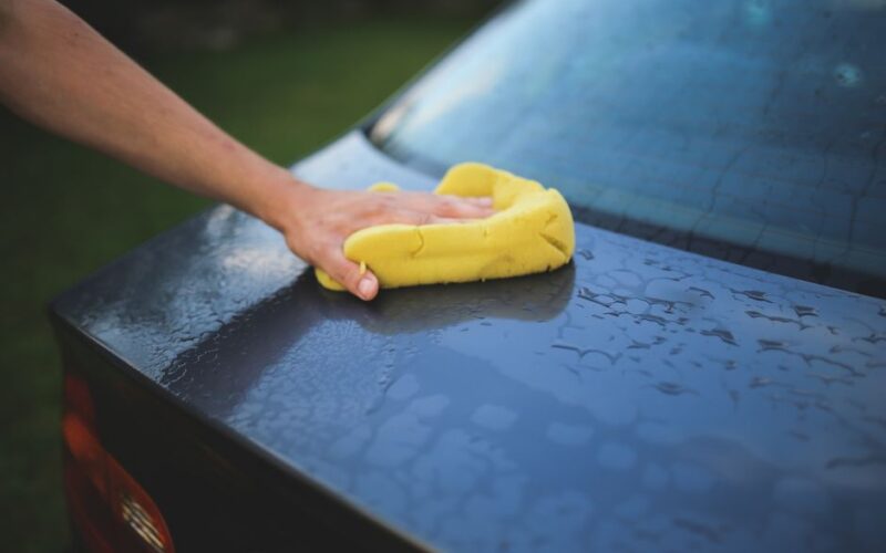 Hand cleaning car with a yellow sponge, showcasing car detailing and washing process.