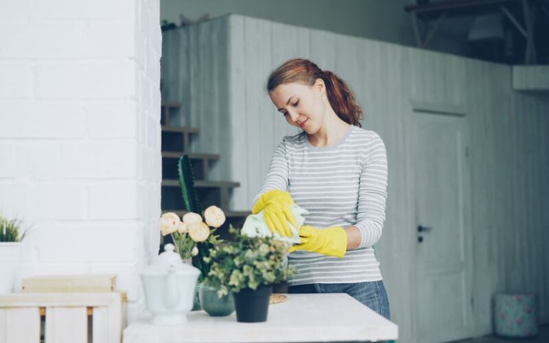 Young woman cleaning home with yellow gloves and striped shirt, focused on tidying indoors.