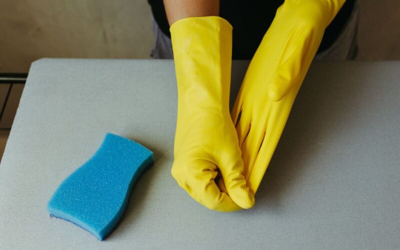 Close-up of hands in yellow gloves preparing for cleaning with blue sponge.
