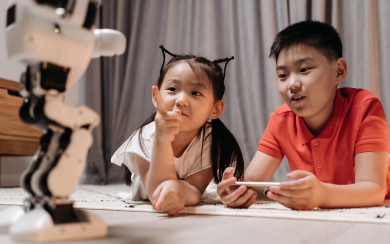 Two children interact with a robotic toy while using a smartphone, showcasing modern technology indoors.