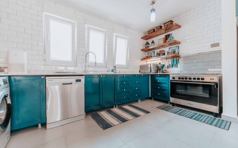 Bright modern kitchen with blue cabinets, stainless steel appliances, and open shelving.