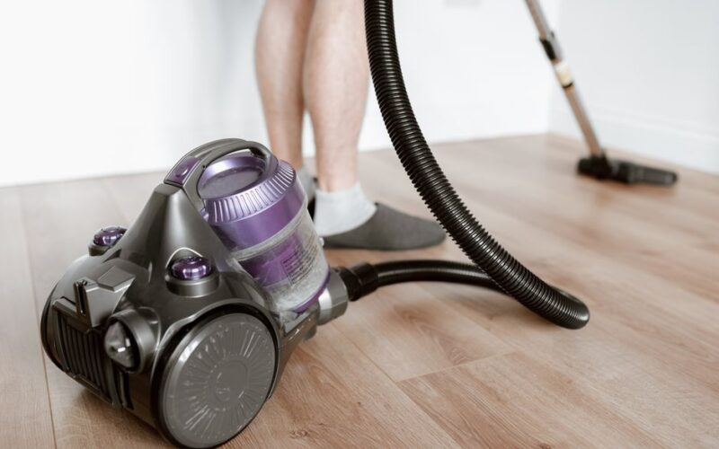 Crop anonymous male tiding flat with modern wireless vacuum cleaner while doing housework