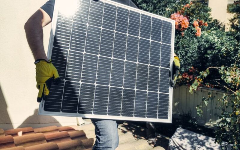 Technician carrying solar panel on rooftop. Clean energy installation outdoors.