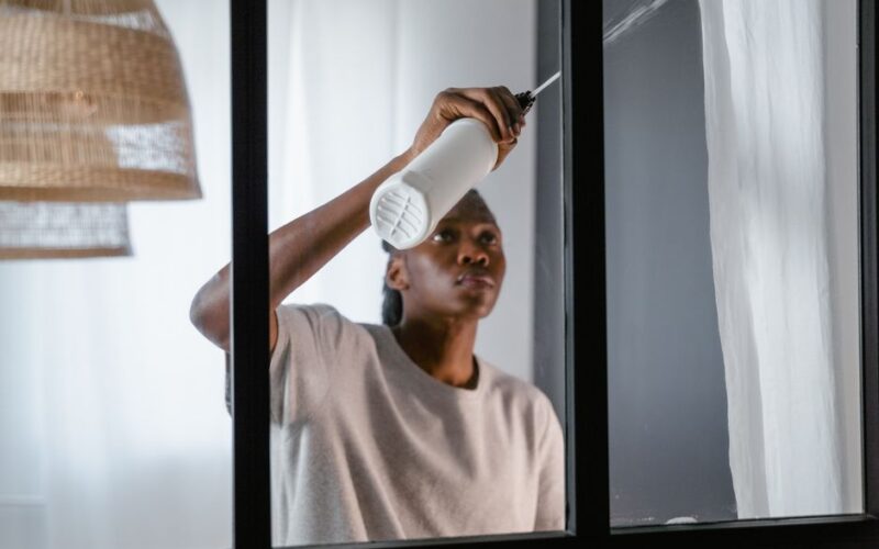 Focused woman using a spray bottle to clean a window with precision.