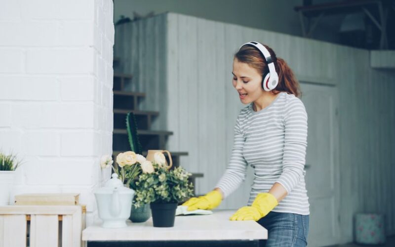 A woman with headphones cleaning indoors, surrounded by plants.