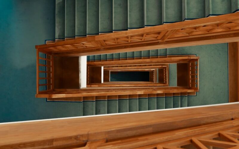 Aerial perspective of an indoor spiral staircase with wooden railings and green carpet.