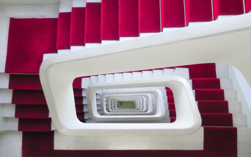Top view of a modern spiral staircase with red carpets and white walls in Lyon.