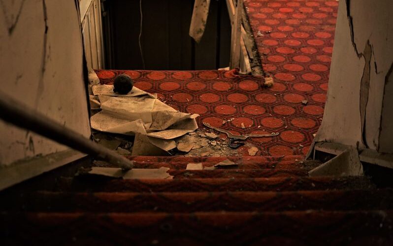 Explore the haunting atmosphere of a neglected, carpeted staircase leading into darkness inside an abandoned building.