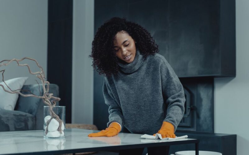 African American woman cleaning a table with orange gloves in a cozy, modern living room setting.