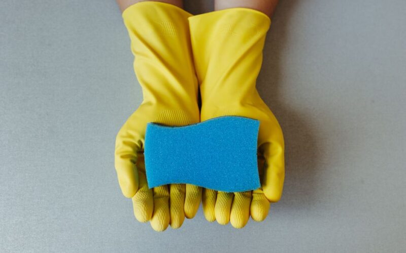 Yellow rubber gloves hold a blue sponge, symbolizing cleaning and hygiene.