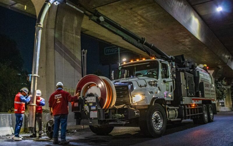 Workers operate a vacuum truck under a bridge at night for city maintenance.