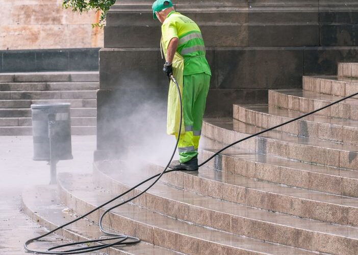 A street worker pressure washes stone stairs in a public park, ensuring cleanliness and safety.