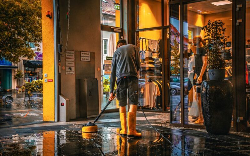 A man cleans the entrance of a store during a rainy day, reflecting urban life.